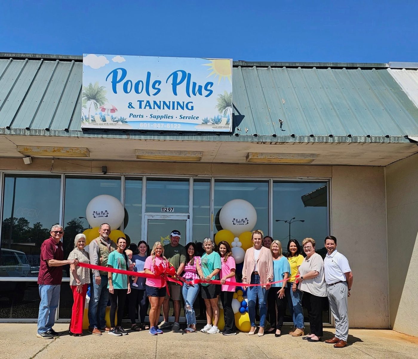 The Pools Plus and Tanning storefront on Old Highway 63, with staff and George County Chamber of Commerce members at the ribbon cutting